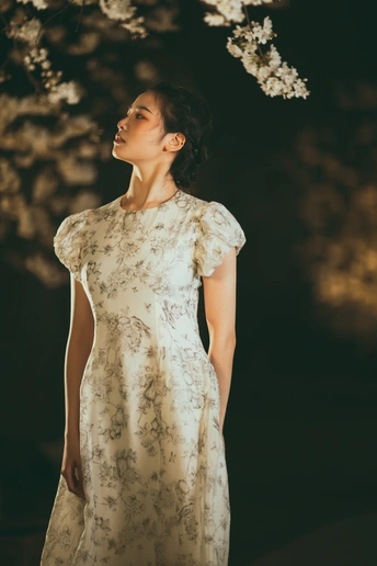 一位穿着花卉连衣裙的年轻女子站在一棵开满花的树上 夜晚时分树上装满了花灯。