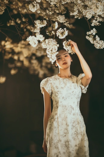 一位穿着白色连衣裙的年轻女子站在一棵点亮的树前 手里拿着花。