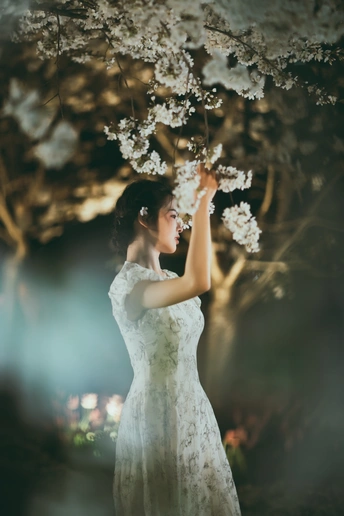 一位穿着白色连衣裙的美女 手持花朵 站在夜晚的森林中。