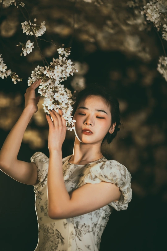 白色连衣裙的年轻女子在树上嗅着白色花朵的肖像