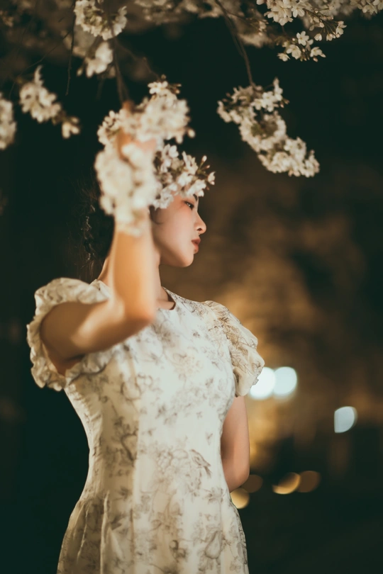 夜晚 一位穿着白色连衣裙的女子在树下拿着花