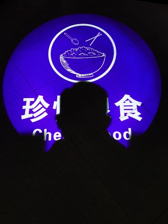 一个男人站在一个带有蓝色氖灯招牌的墙前