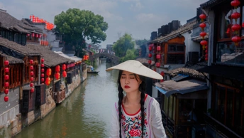 一个戴着帽子的女人站在一条有船的河边