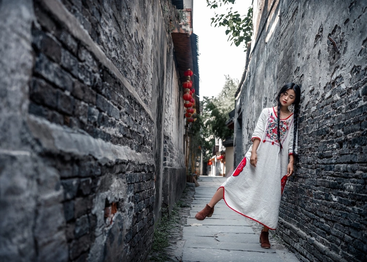 一个穿着白色连衣裙的年轻女子走在一条狭窄的小巷里