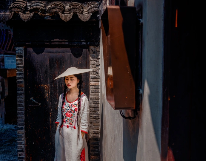 一个穿着传统服装的年轻女子撑着伞站在老建筑之间的小巷里