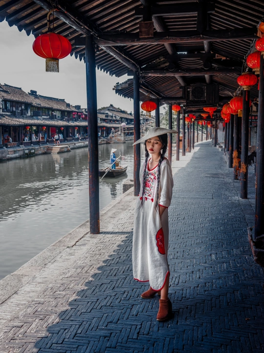 一个穿着和服、戴着帽子的女人提着红灯笼沿着运河走