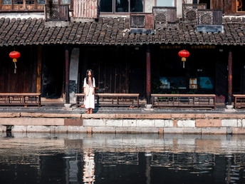 一个穿着白色连衣裙的女人站在一座水面上有红色的旧建筑前