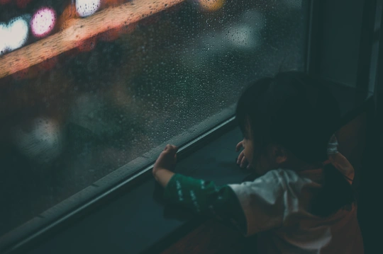 一个小女孩和一个男孩在雨中公交车上看着窗外