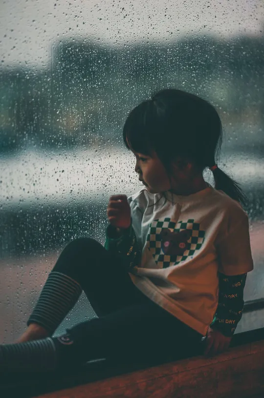 一个小女孩坐在窗台上 向外望着雨。