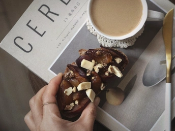 一个人在桌子上拿着一个装有坚果和巧克力的甜甜圈和一杯咖啡