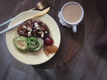 木桌上放着一盘白色的食物 旁边放着一杯咖啡、一把叉子和一份水果蔬菜沙拉