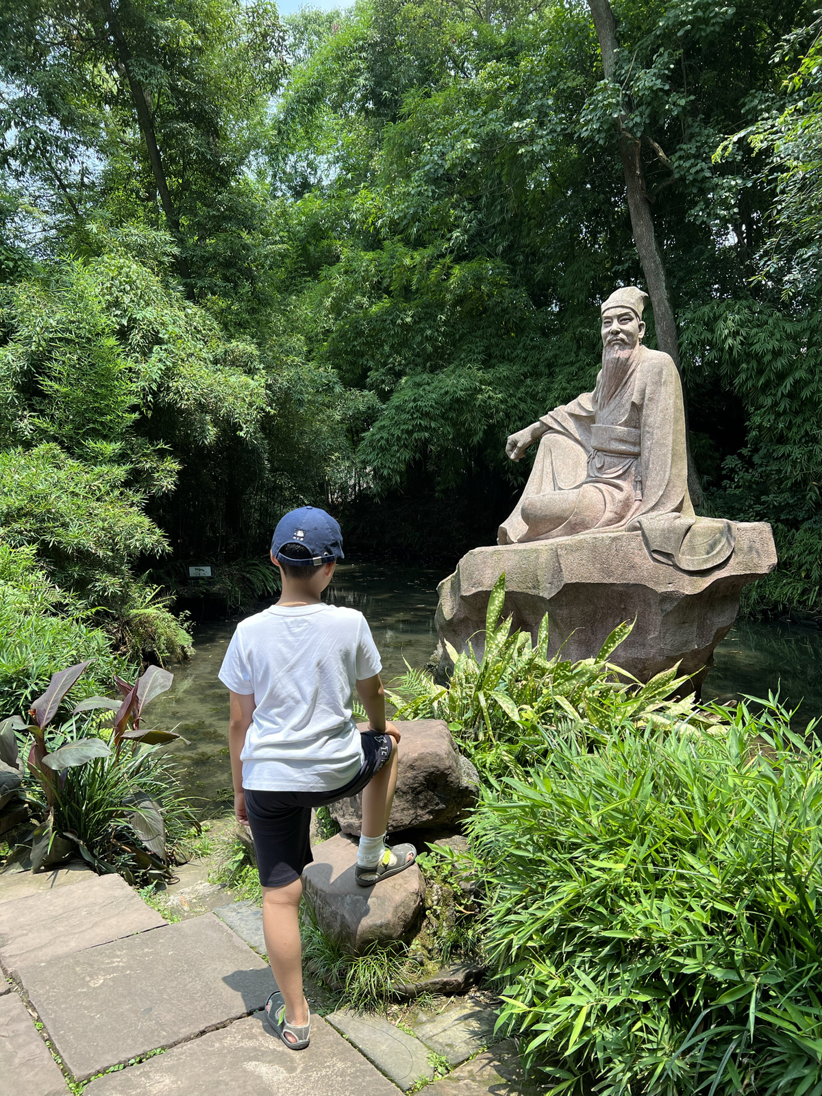 一个男人站在岩石上看着花园池塘里的雕像