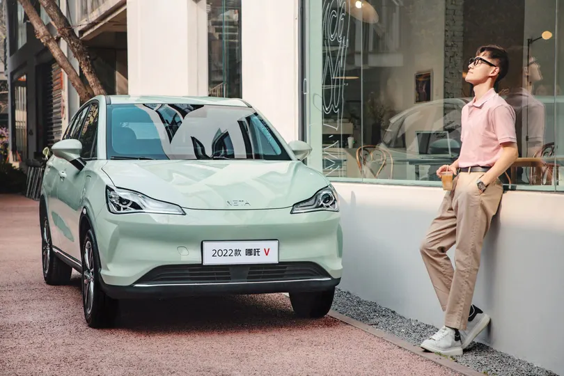 一位妇女站在商店窗户外面 外面停着一辆小绿车 一名男子靠在窗户上。