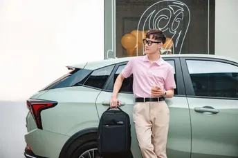 站在一辆绿色汽车旁边 一个年轻人拿着一个手提箱。