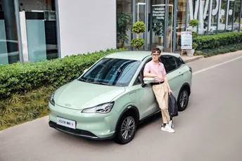 一位站在街边的小型绿色汽车旁的女士