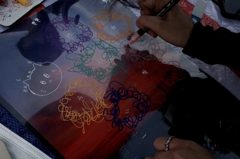 一位妇女在桌子上剪一幅画 而一位剪子手在画板上工作 一位男子正在画一幅画。