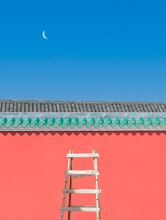 一根倾斜的木材梯子靠在红色墙壁上 背景是蓝色的天空和月亮。