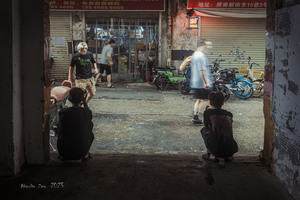 夜晚的一个小巷子里 有些人坐在地上 一个男人经过一家商店。
