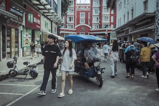 一个人群正在沿着有遮阳伞的建筑物附近的街道行走。