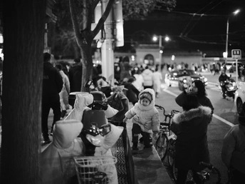 一张黑白照片 夜晚街道 人群 小女孩骑自行车。