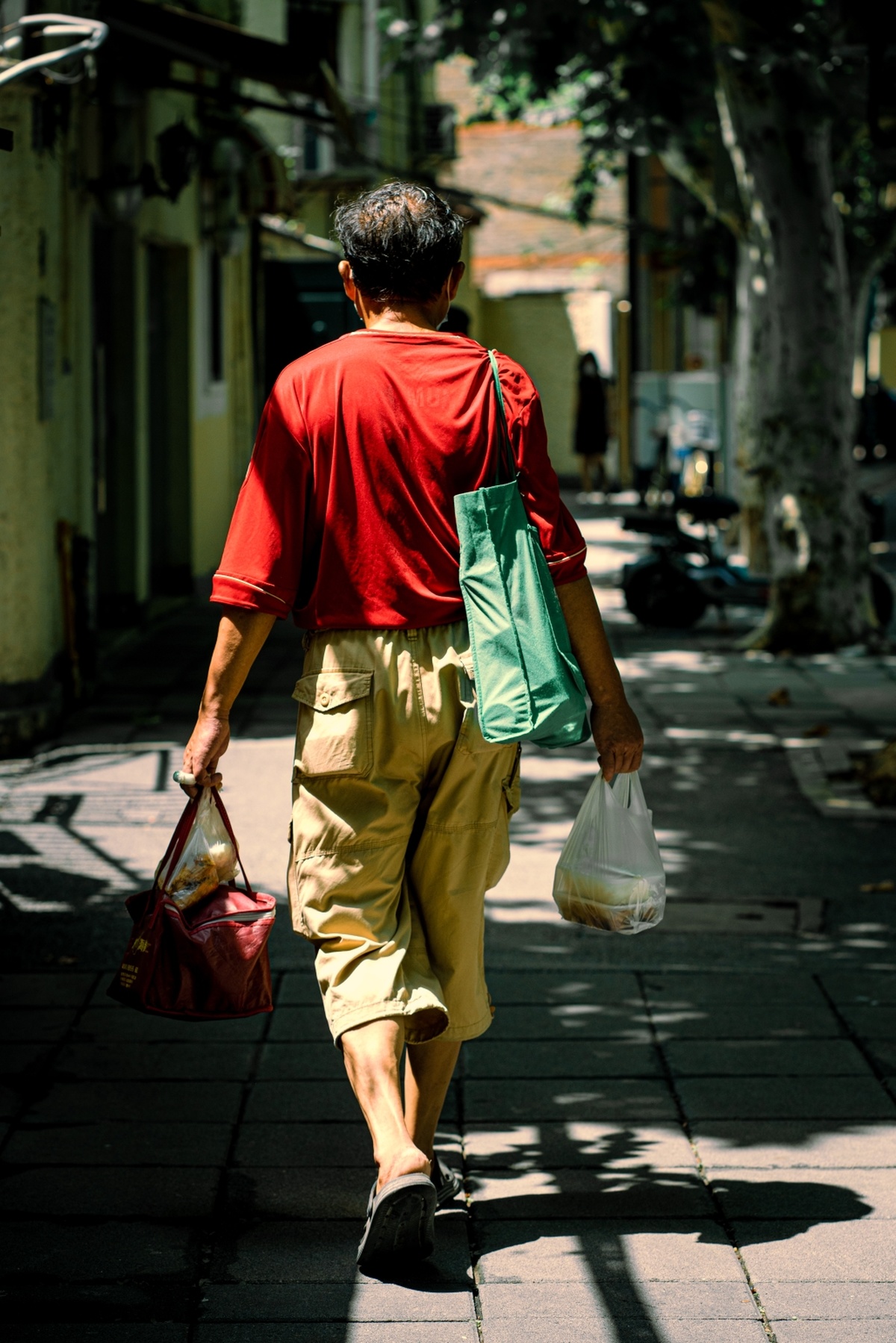 一个穿着红色衬衫和卡其色裤子的男人手里拿着购物袋走在街上