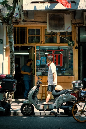 一名男子站在一家商店前 前面停着一辆轻便摩托车 人们在街上的人行道上走来走去