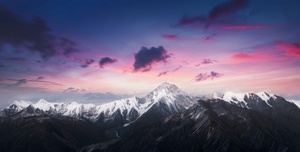 美丽的夕阳 落在白雪皑皑的山上 上方有紫色的和粉色的云彩。