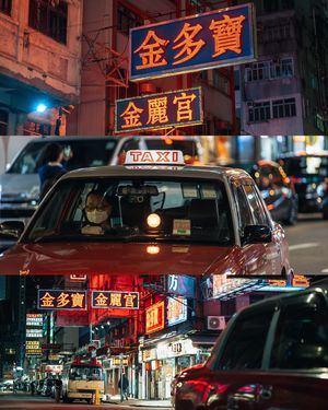 夜晚 一辆红色的出租车驶过繁忙的街道 街道两旁是亮着灯的建筑和霓虹灯的招牌。