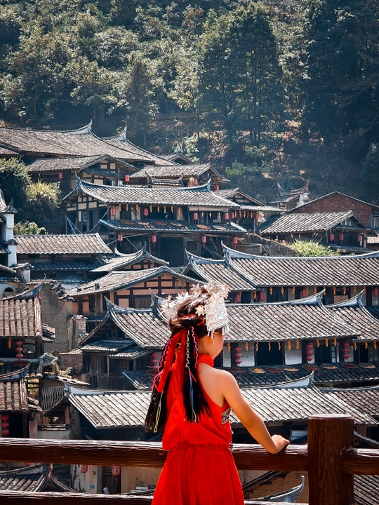 一位穿着红裙子的女人站在一座村庄的建筑物前