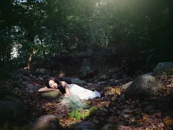 一位美丽的年轻女士穿着白色连衣裙躺在森林中的一块岩石上