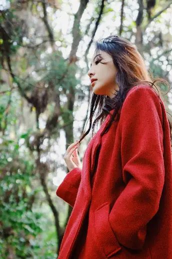 一位穿着红色外套的女士站在一棵棵树木组成的森林中