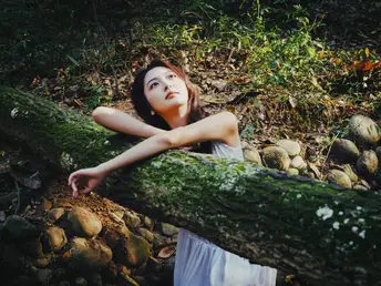 美丽的年轻女子穿着白色连衣裙躺在森林中的岩石上