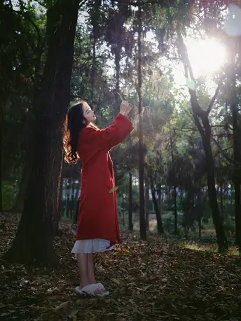 一位穿着红裙子的年轻女子站在森林中 阳光透过树木洒下