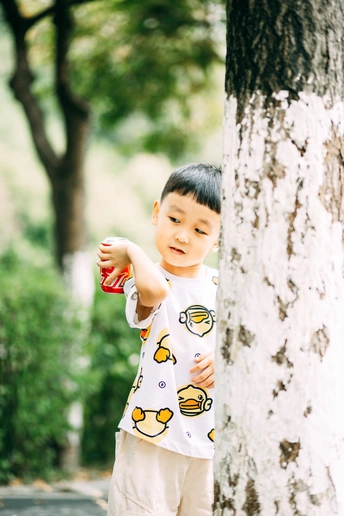 一个小男孩拿着一个小杯子站在公园里的一棵树旁