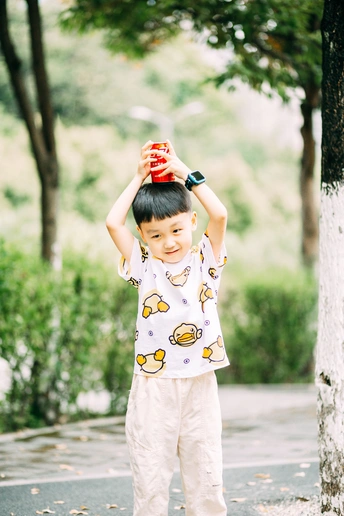 一个穿着睡衣的小男孩站在街上一棵树旁的滑板上 双手捂着头