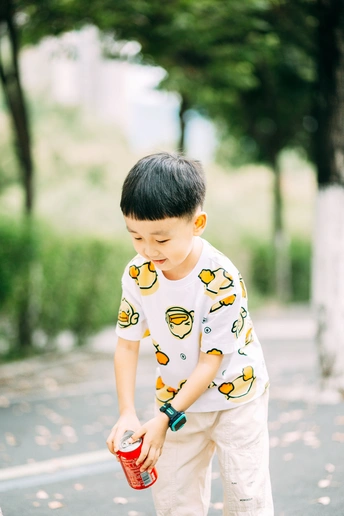 一个骑着滑板的小男孩站在人行道上 手里拿着杯子和罐子