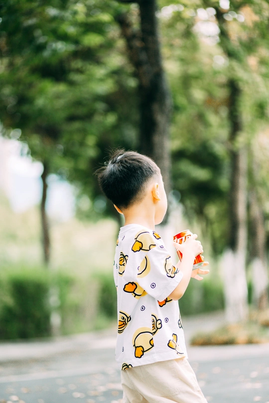 一个手里拿着滑板的小男孩站在公园的路中央 一个小男孩把手放在滑板上