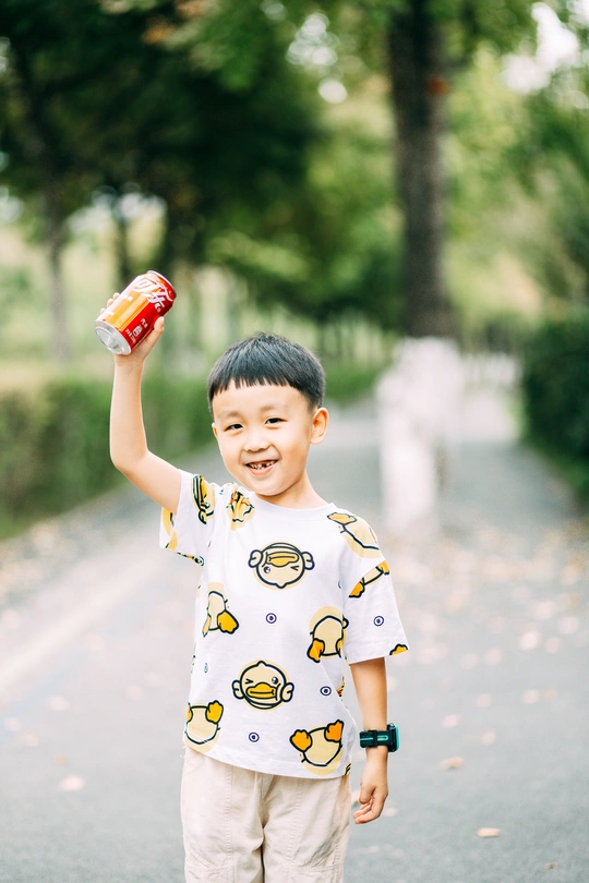 站在公园里铺好的路上 手里拿着一个小瓶或饮料的小男孩