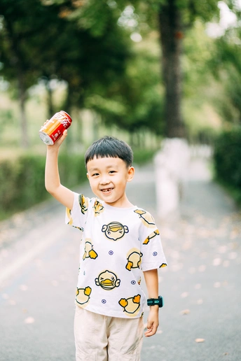 站在公园里铺好的路上 手里拿着一个小瓶或饮料的小男孩