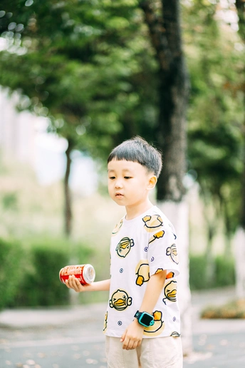 一个穿着睡衣的小男孩拿着杯子和罐子站在街上的滑板上