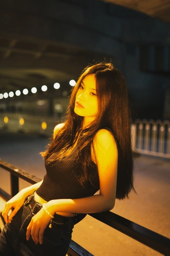 一个美丽的年轻女子坐在夜晚的台阶上 桥下有灯光。