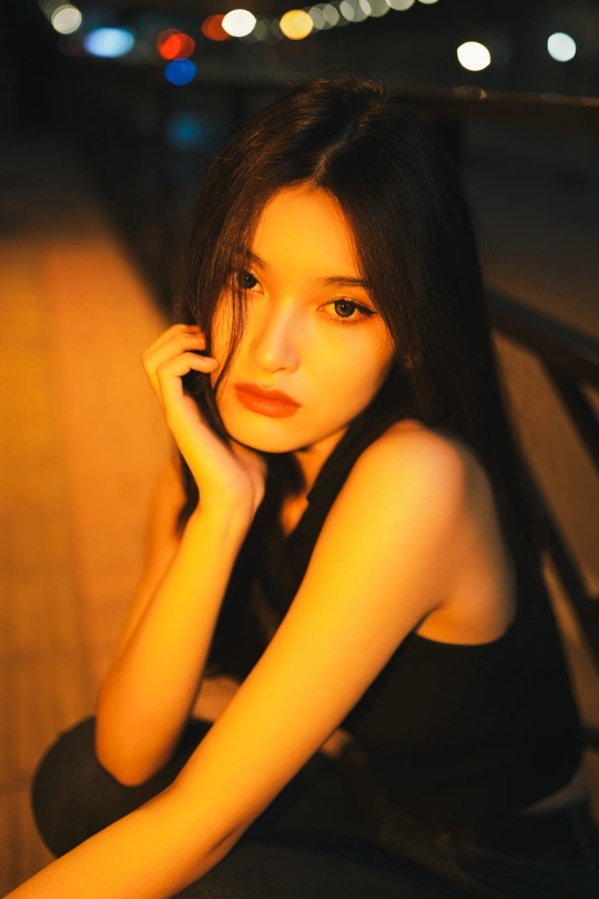 一个年轻女子坐在夜晚的长椅上 背景有灯光。