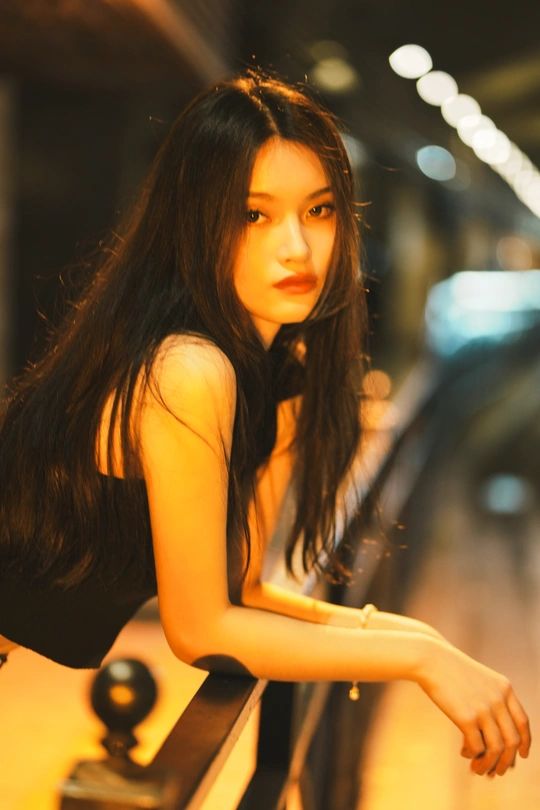 一个穿着黑色连衣裙的年轻女子坐在地铁站的铁轨上 背景中有一辆火车。