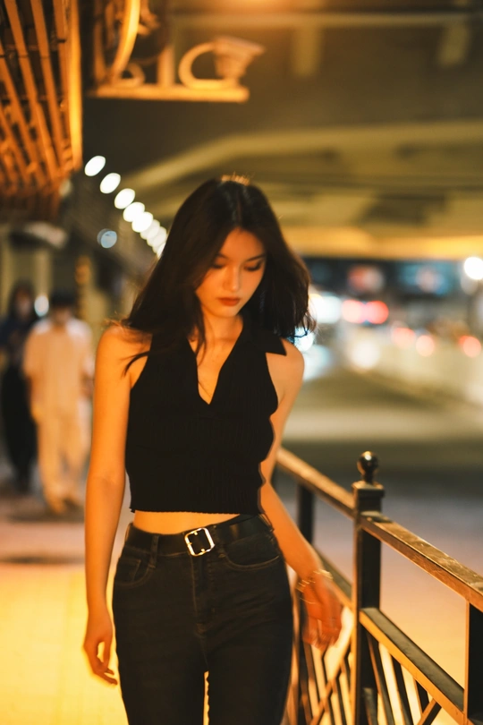 一位穿着黑色上衣和牛仔裤的年轻女子站在街头。