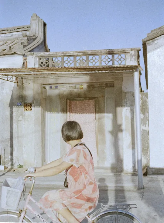 一个穿粉色裙子的女孩骑自行车经过一所老房子