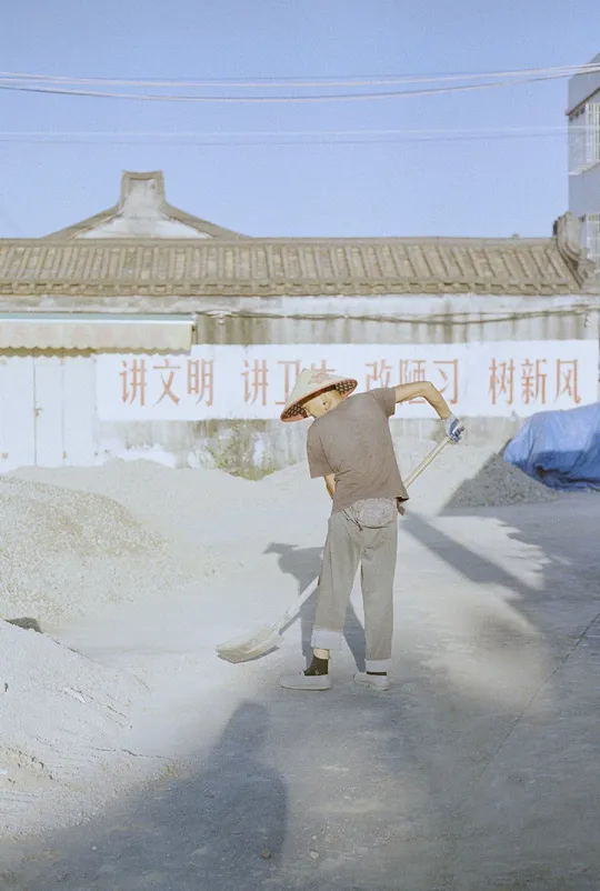 一个男人拿着铲子走在大街上 前面有一栋建筑。