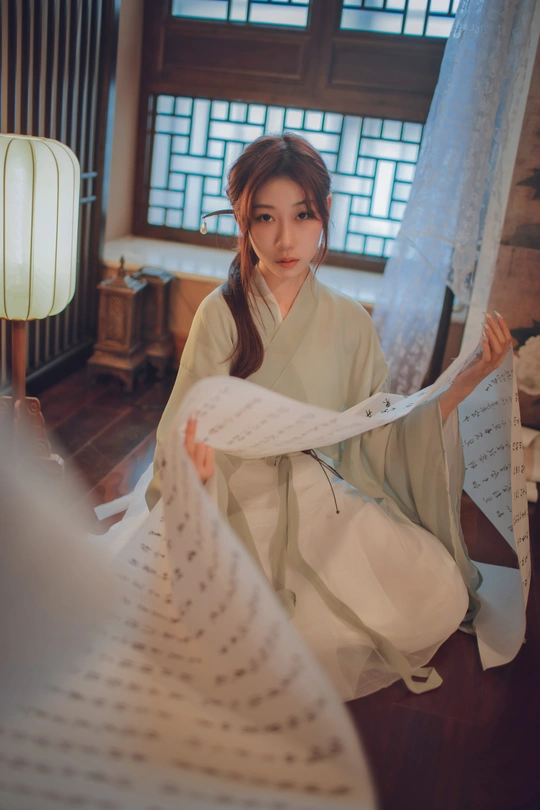 一个穿着传统和服的年轻女子在地板上拿着一张白纸