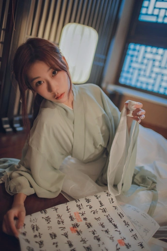 一个穿着白色长袍的年轻女子坐在床上拿着一张纸