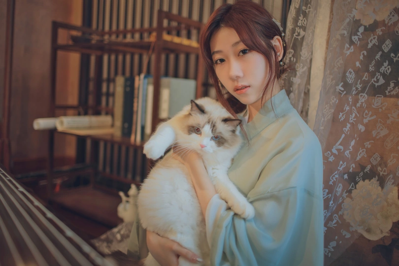 一个穿着蓝色连衣裙的年轻女子抱着一只白猫