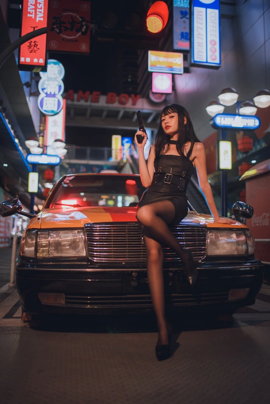 一个年轻女人晚上坐在一辆黑色汽车的引擎盖上